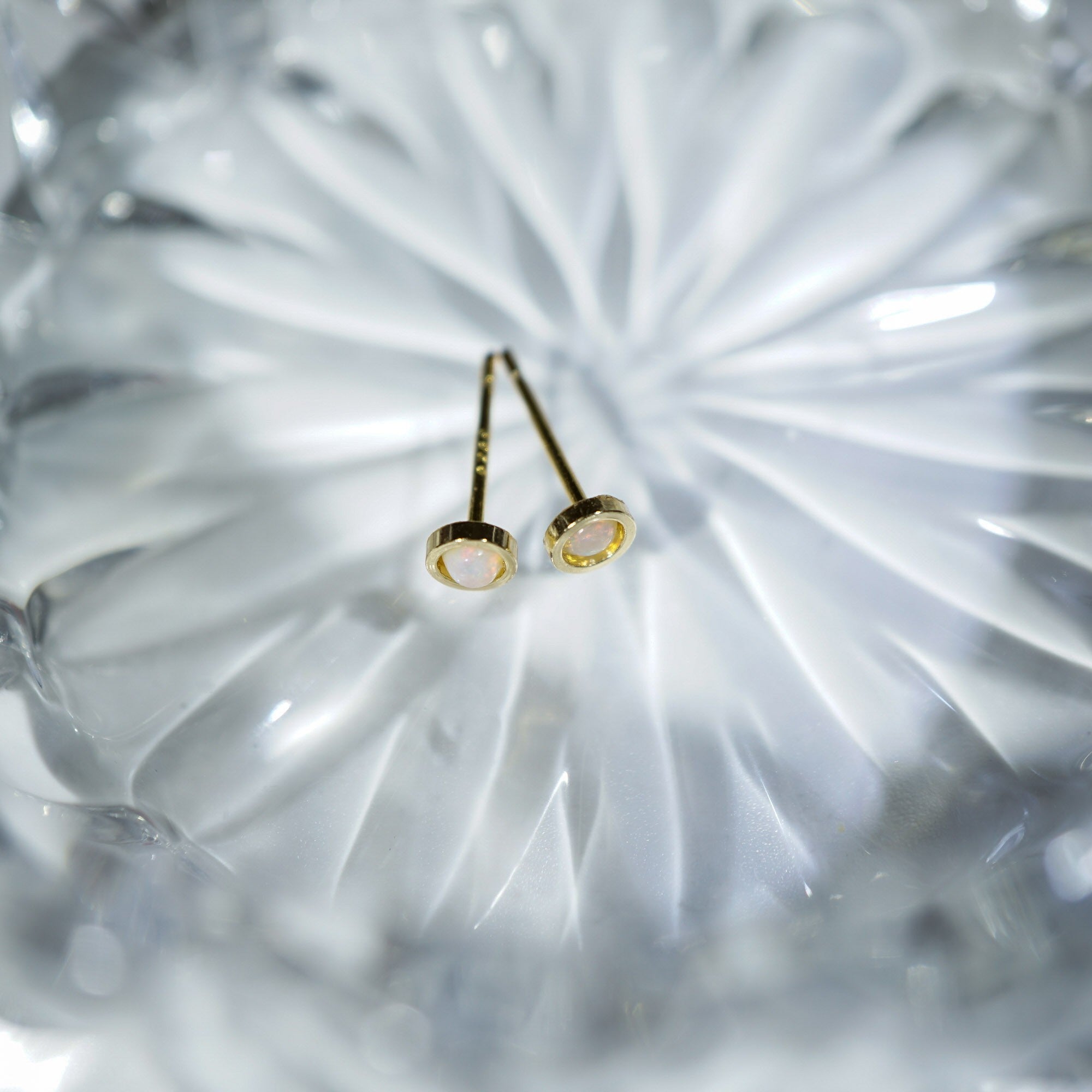 A pair of gold post earrings with oval milky white stones, resting on a textured, faceted clear glass surface.