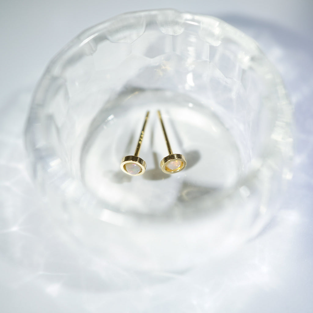 A pair of gold post earrings with oval white inlays, resting inside a clear textured glass dish on a white surface.