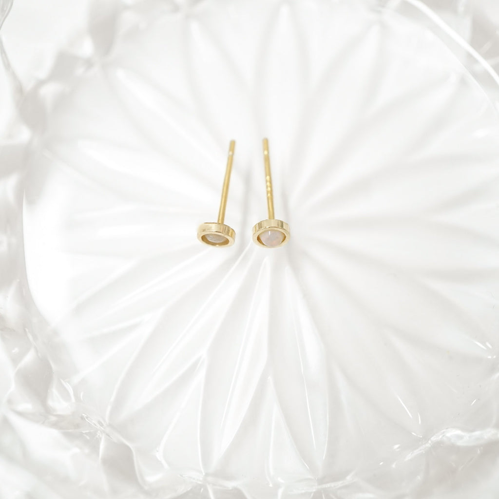 A pair of gold post earrings with oval mother-of-pearl inlays, displayed on a textured white glass plate.
