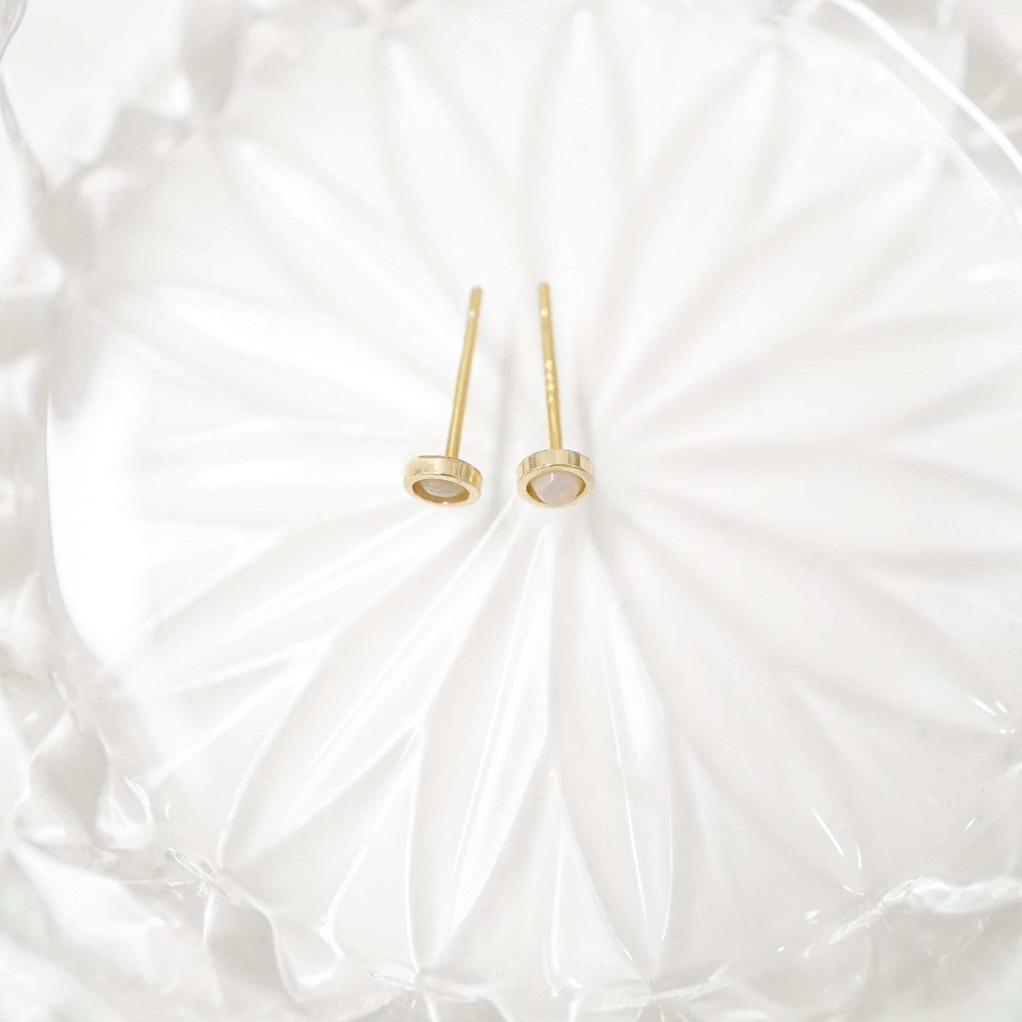 A pair of gold post earrings with oval mother-of-pearl inlays, displayed on a textured white glass plate.