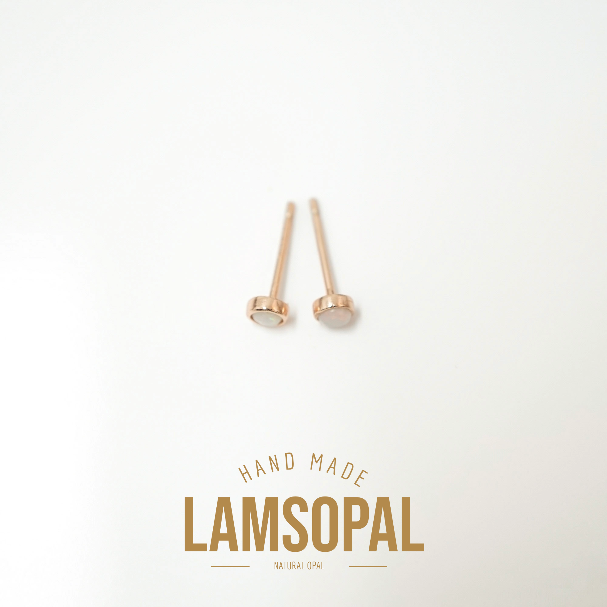 A pair of rose gold stud earrings with flat circular faces, displayed on a clean white background with a gold text overlay that reads 'HAND MADE LAMSOPAL NATURAL OPAL'.