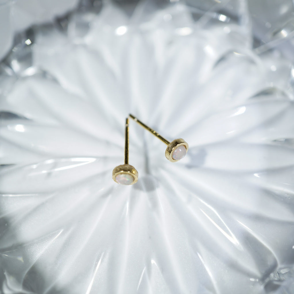 A pair of gold post earrings with oval white stones, displayed on a textured white glass plate.