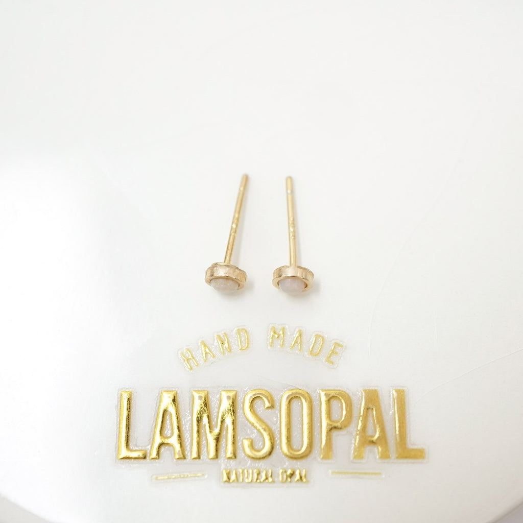 A pair of gold post earrings with oval bezel-set pale pink stones, displayed on a white surface above a gold 'HAND MADE LAMSOPAL' logo.