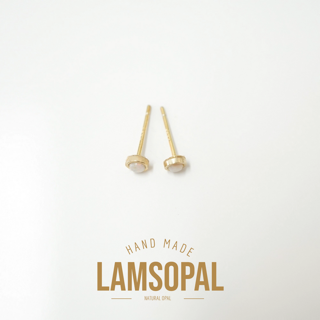 A pair of small gold stud earrings with oval clear stones on a white background, with the text 'HAND MADE LAMSOPAL NATURAL OPAL' printed below.