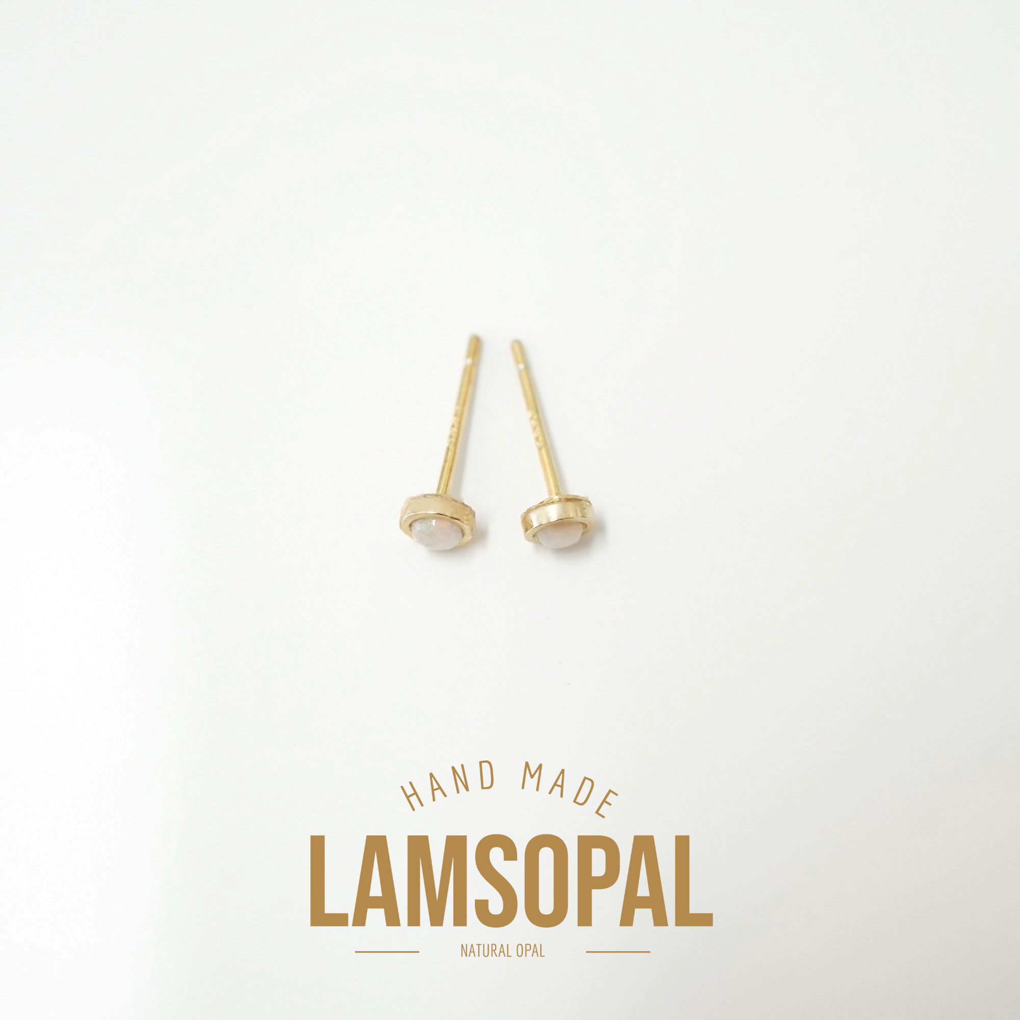 A pair of small gold stud earrings with oval clear stones on a white background, with the text 'HAND MADE LAMSOPAL NATURAL OPAL' printed below.