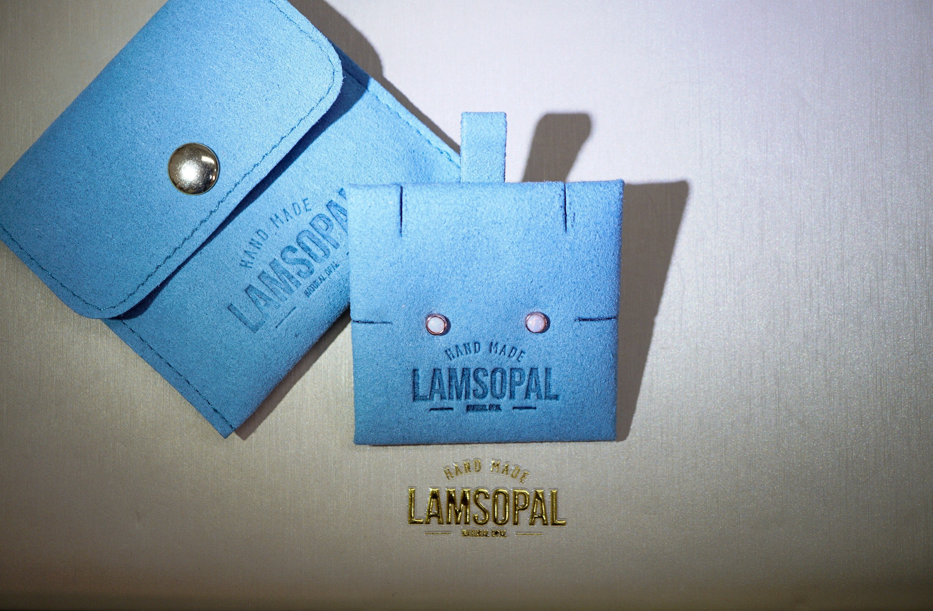 A light blue leather wallet and matching card holder with the brand name LAMSOPAL, displayed on a textured beige background.