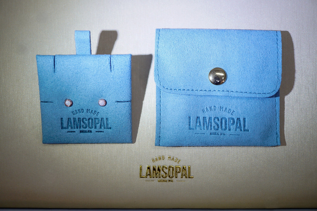 A pair of light blue handmade leather card holders or wallet-like accessories with the brand name LAMSOPAL embossed on them, displayed on a beige background.