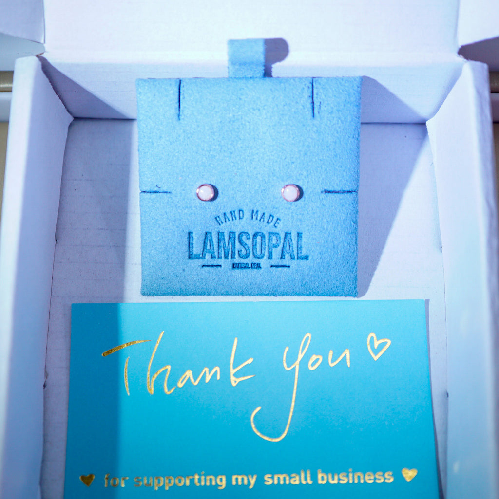 A small blue textured jewelry box or display insert with the words 'HAND MADE LAMSOPAL' printed on it, placed inside a white box next to a turquoise thank-you card with gold script reading 'Thank you' and 'i'm supporting my small business'.