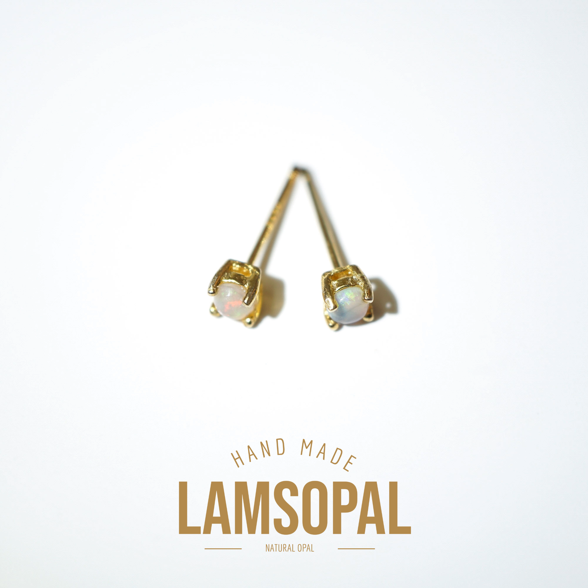 A pair of gold stud earrings with round iridescent opal gemstones, displayed on a clean white background with a gold 'LAMSOPAL' brand logo and 'HAND MADE' text below.