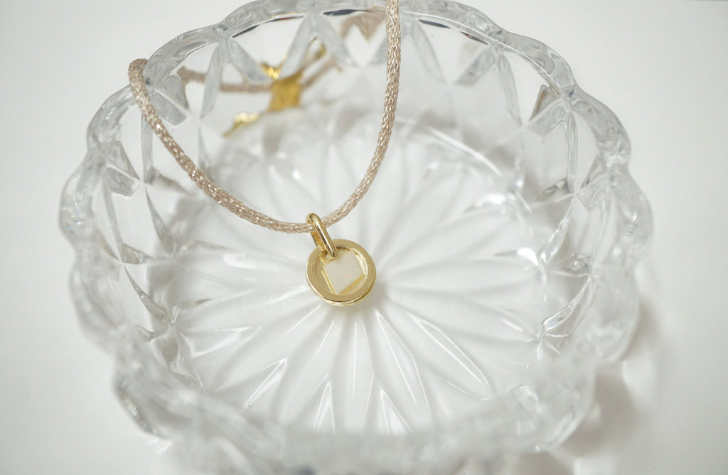 A delicate gold chain necklace with a small gold ring pendant, displayed inside a clear faceted glass bowl on a white background.