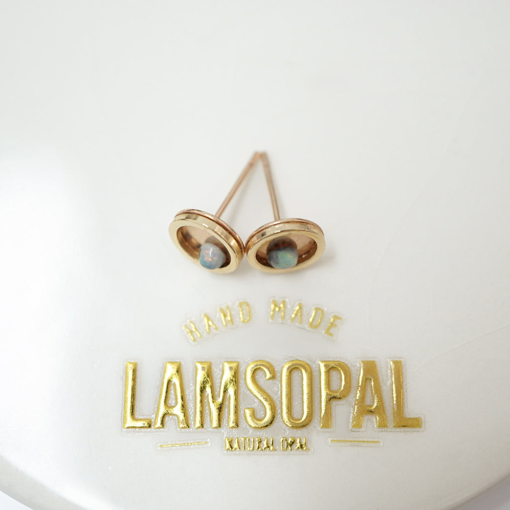 A pair of gold-toned oval stud earrings with small natural opal inlays, displayed on a white surface above gold foil text reading 'HAND MADE LAMSOPAL'.