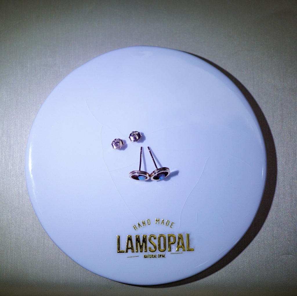 A pair of rose gold stud earrings with clear round-cut stones and matching backings, displayed on a white circular branded card that reads 'HAND MADE LAMSOPAL'.