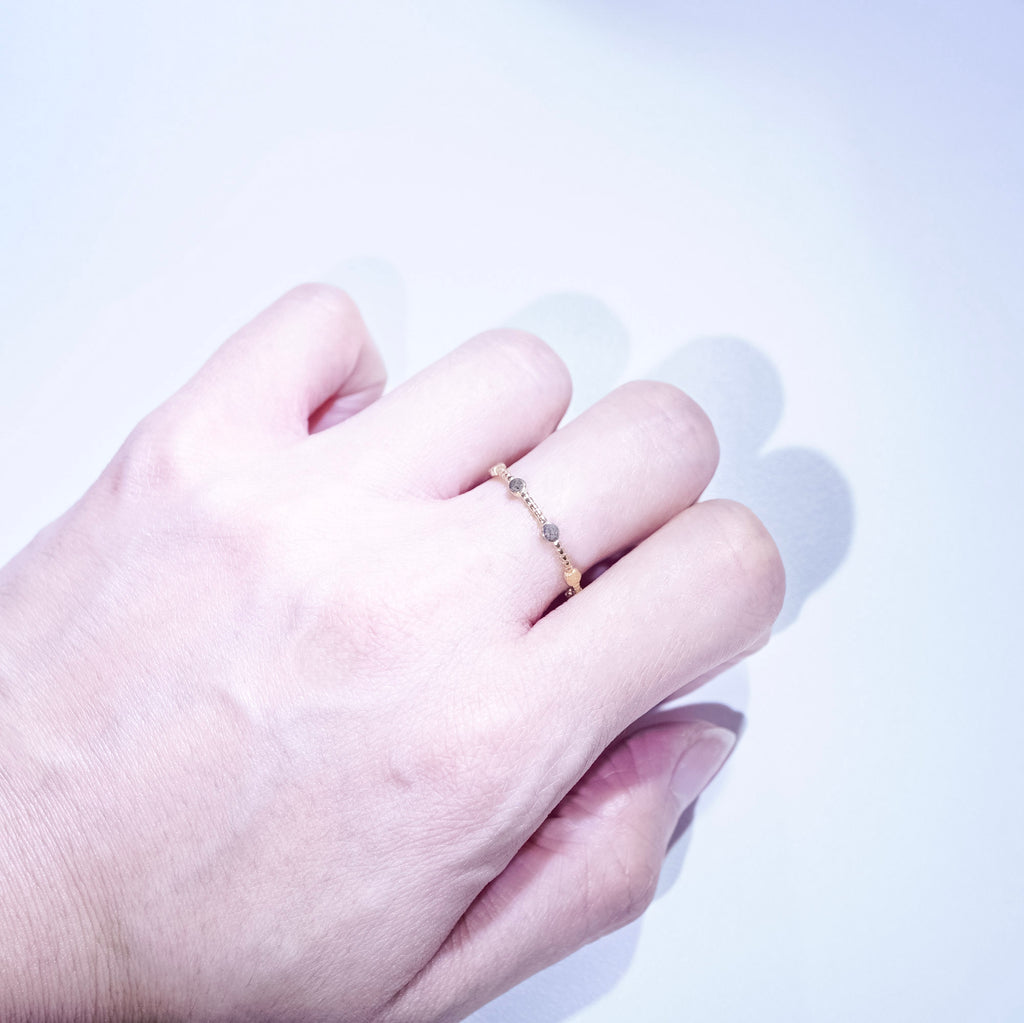 A close-up of a hand wearing a delicate gold ring with small clear stones on a light, clean background.