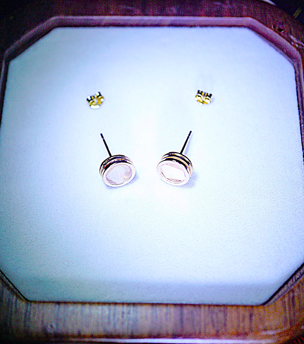 A pair of gold stud earrings with oval-cut clear stones in silver-toned settings, displayed on a white insert inside an octagonal wooden jewelry box.