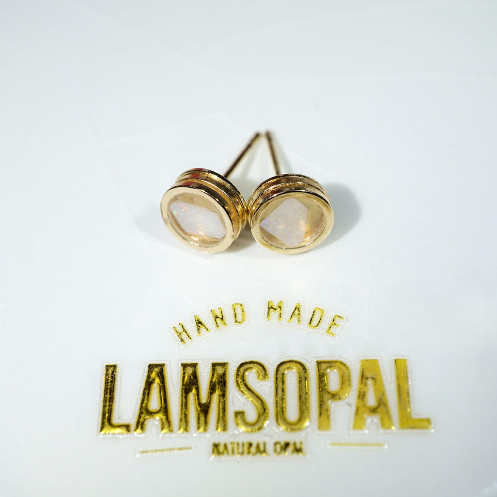 A pair of gold stud earrings with oval milky white inlays, displayed on a white surface above a gold foil brand label that reads 'LAMSOPAL'.