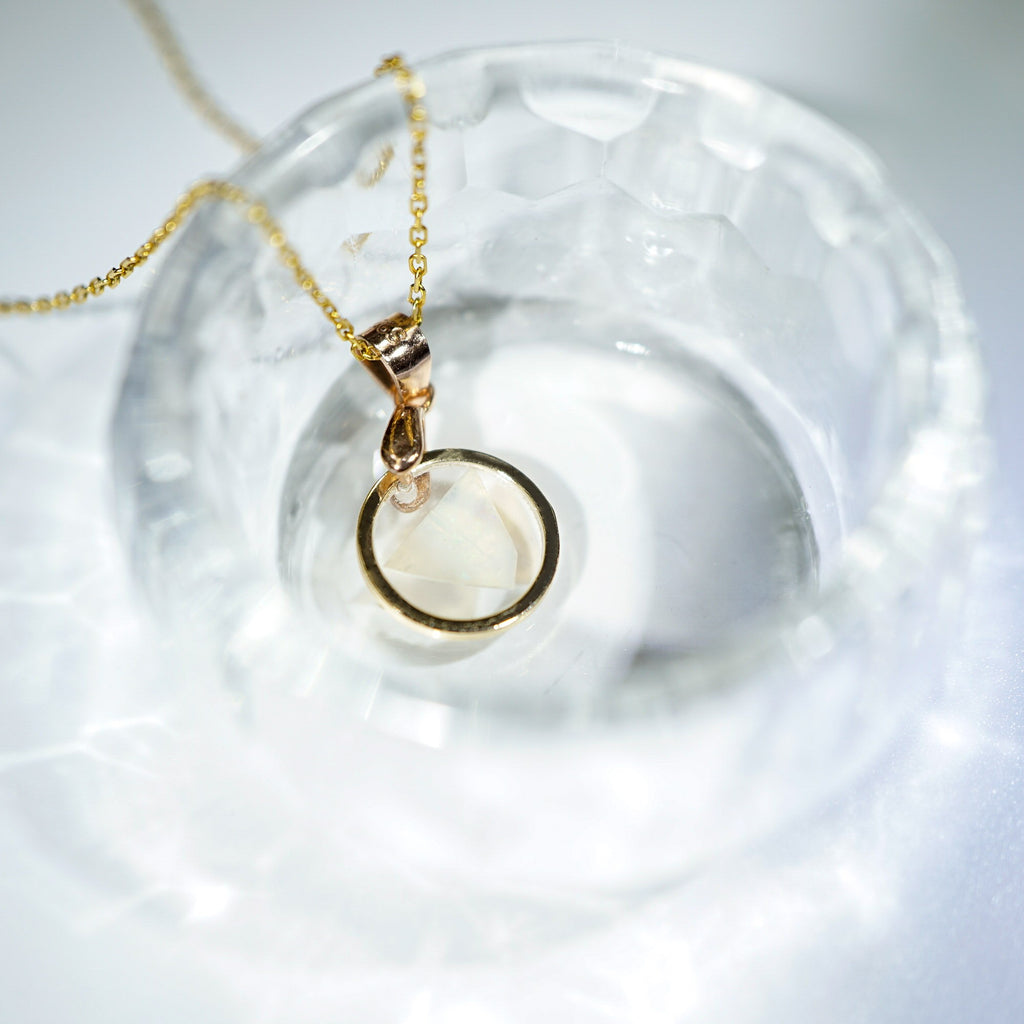 A gold necklace with a circular pendant resting inside a textured clear glass bowl on a white surface.
