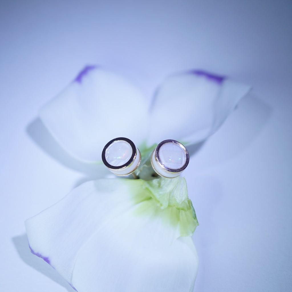 A pair of silver-toned stud earrings with oval clear gemstones, displayed on white flower petals against a soft light blue background.