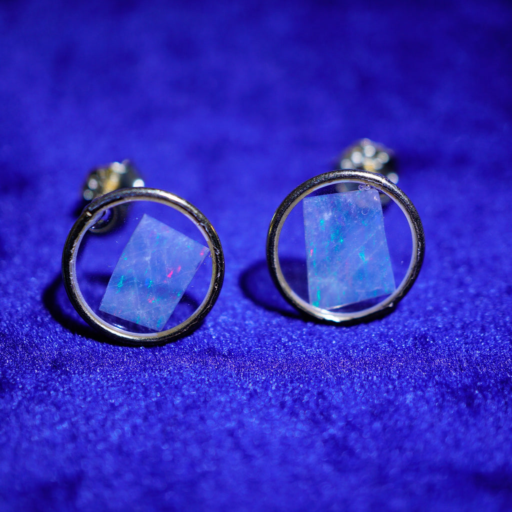 A pair of silver-toned circular stud earrings with faceted blue iridescent opal-like centers, displayed on a textured royal blue velvet surface.