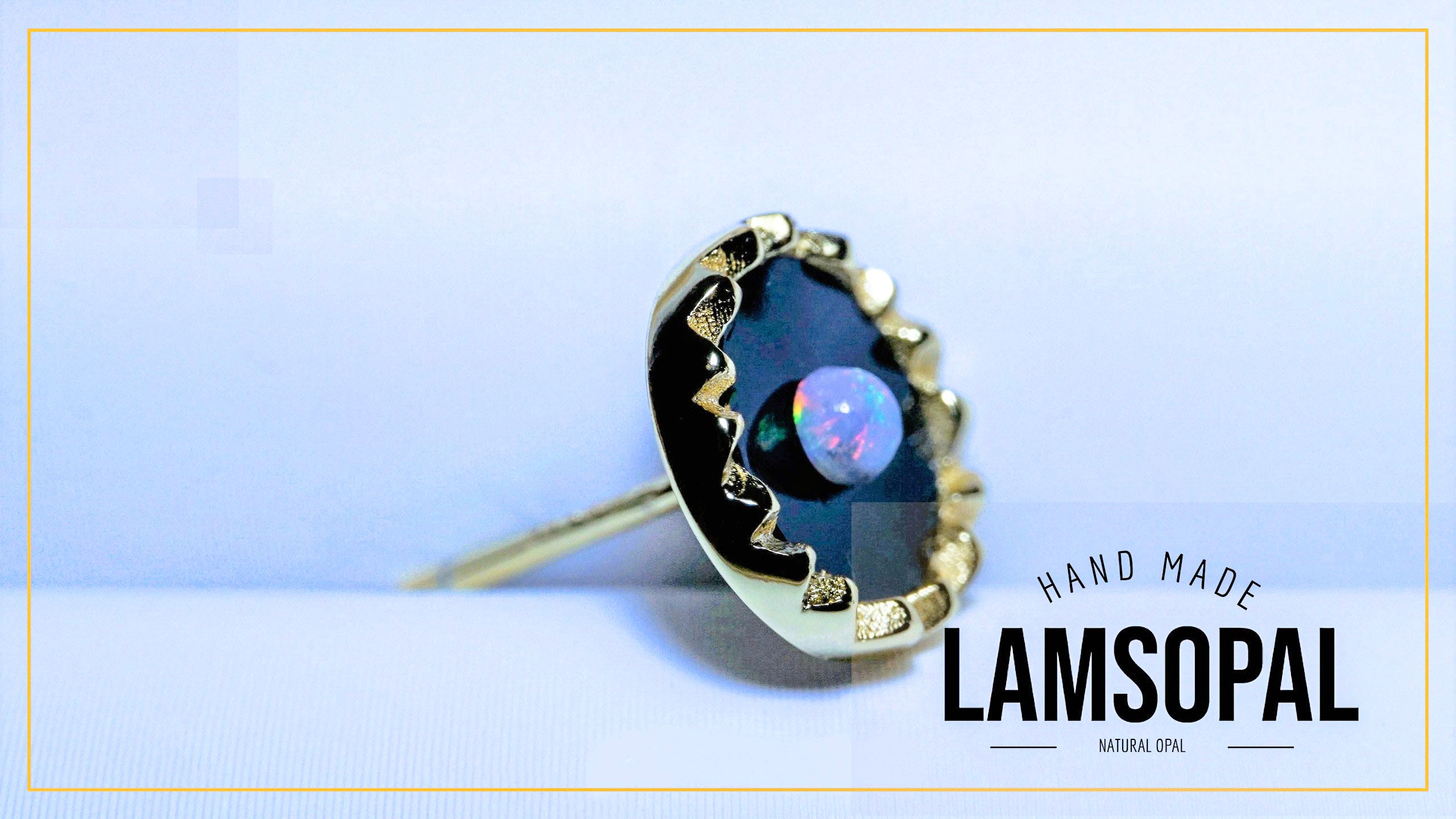 A handmade Lamsopal natural opal ring with a gold-toned bezel setting and a dark blue iridescent opal stone, shown on a light blue background with a gold border and text overlay.