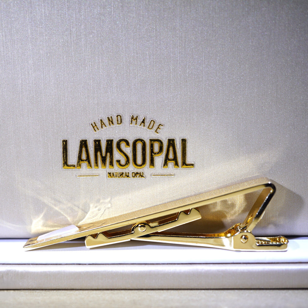 A gold tie clip displayed on a white textured background with the brand name 'LAMSOPAL' printed above it.