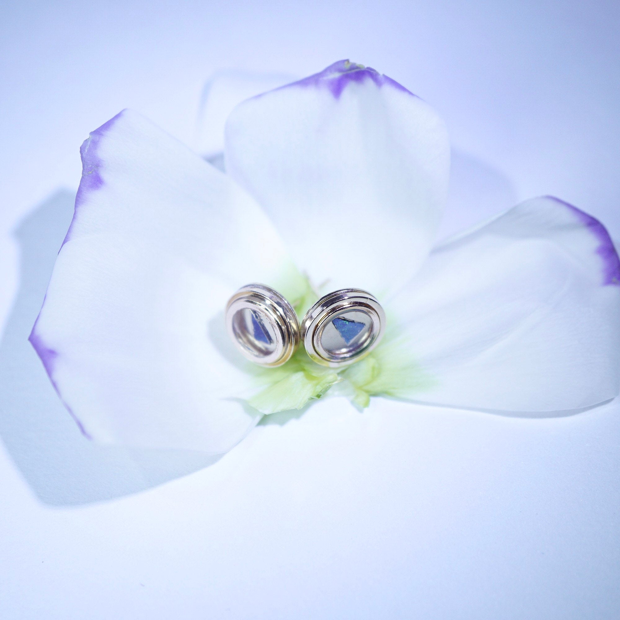 Silver earrings on a white flower with a purple petal against a light purple background