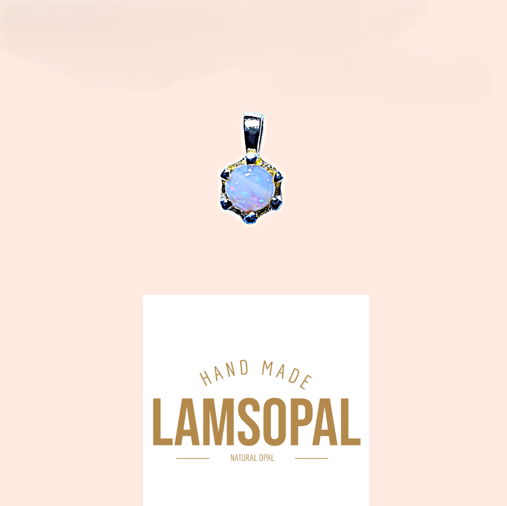 A silver pendant with a round iridescent blue opal center and small dark blue stones, shown above a white card that reads 'HAND MADE LAMSOPAL NATURAL OPAL' on a pale peach background.