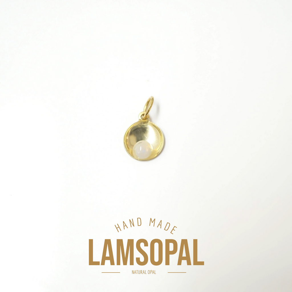 A small gold pendant charm with a natural white opal in a half-circle setting, displayed on a clean white background with 'HAND MADE LAMSOPAL NATURAL OPAL' text below.