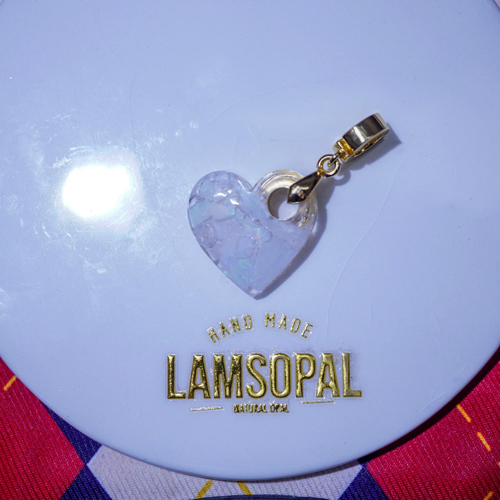Heart-shaped pendant with gold clasp on a LAMSOPAL branded circular object