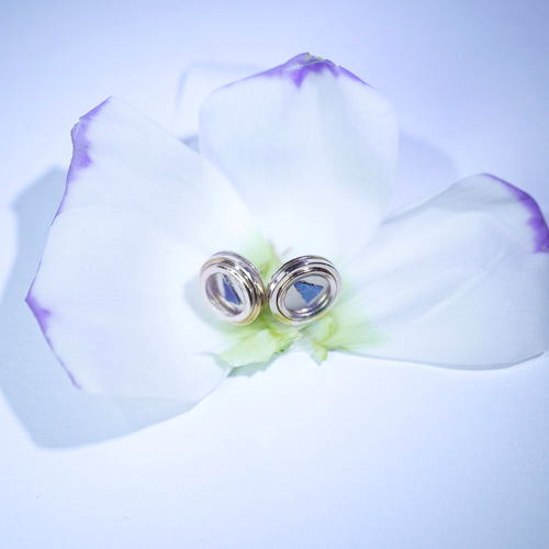 Opal earrings on a white flower with a purple petal against a light purple background