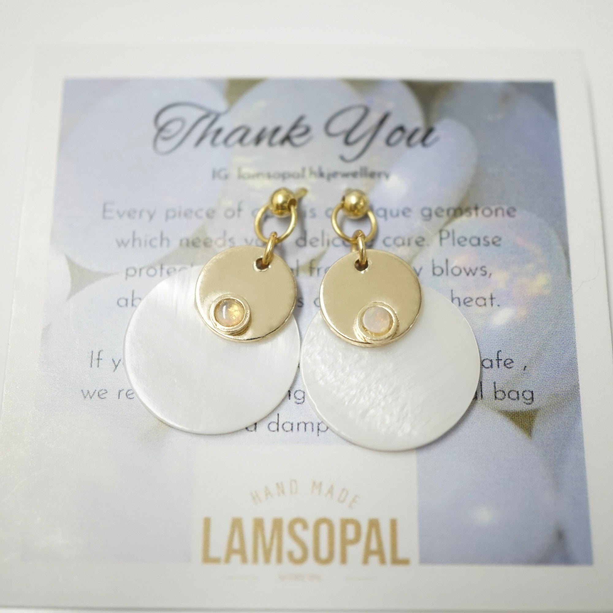 A pair of Lamsopal handmade earrings with gold-toned circular discs and white disc pendants, presented on a branded white and blue card with a 'Thank You' message.