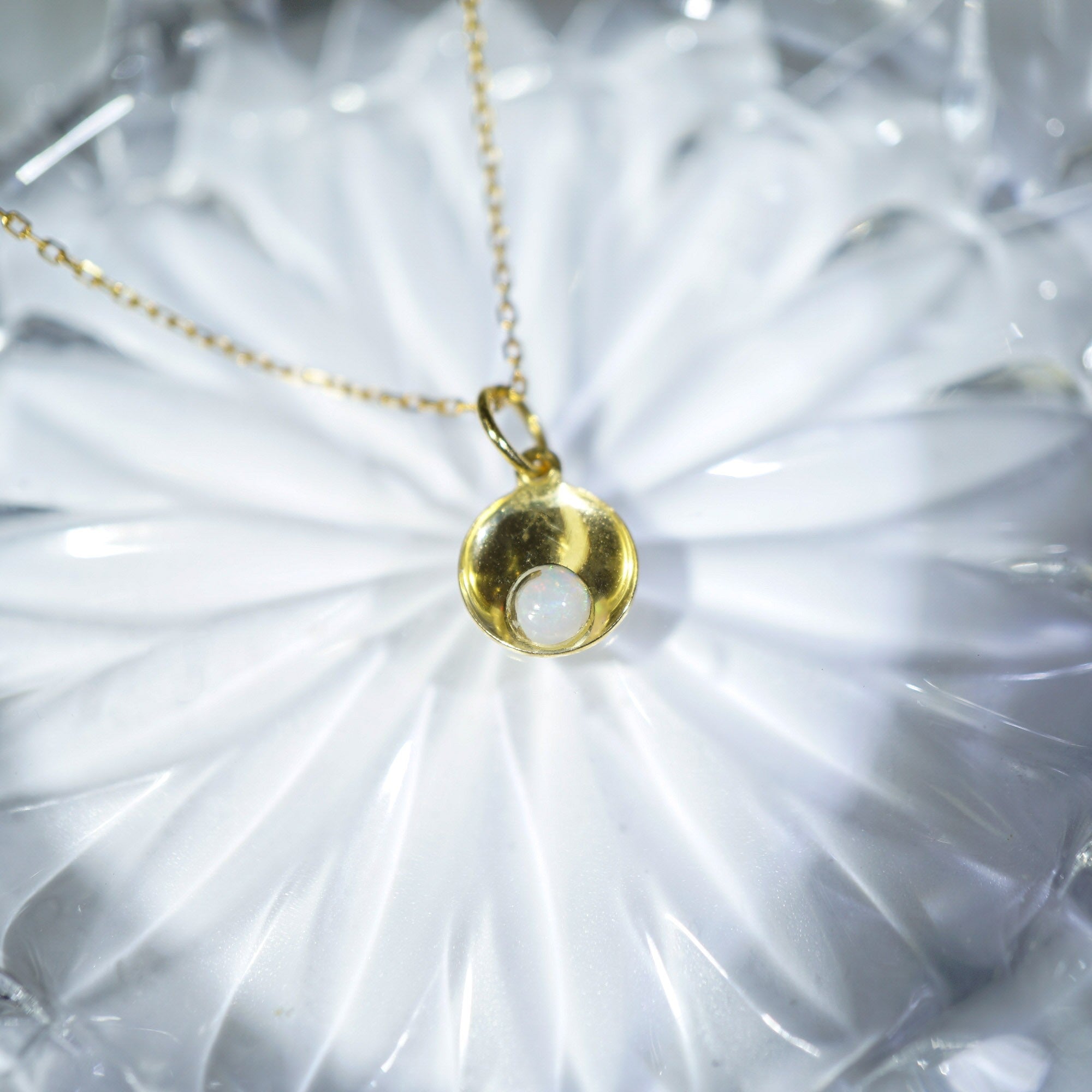 A gold pendant necklace with a polished crescent moon design and a white circular inlay, resting on a white textured surface.