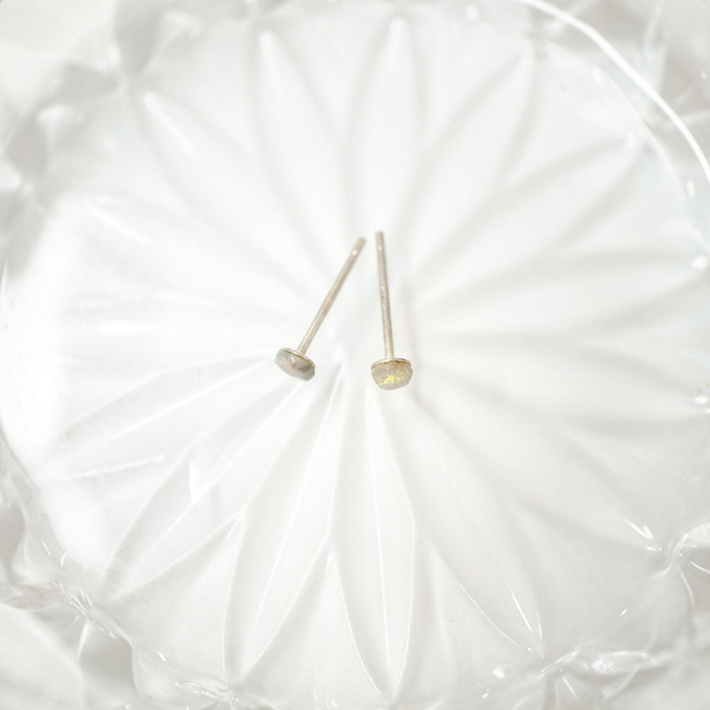 Two small gold-toned stud earrings with flat oval discs on thin posts, resting on a white textured glass dish.