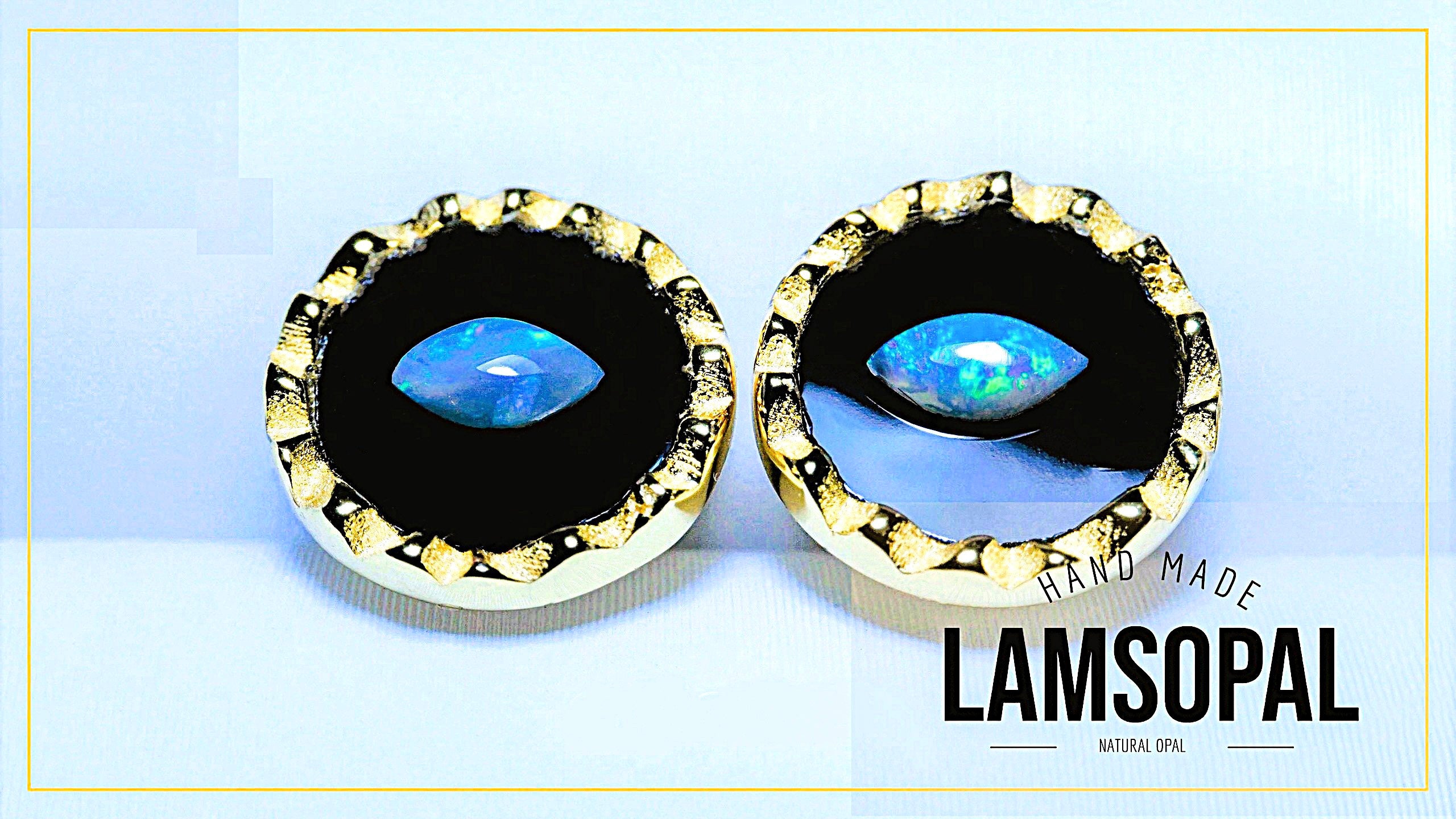 A pair of handmade Lamsopal natural opal earrings with round bezel-set blue opal stones in black and gold settings, displayed on a light blue background with a gold border.