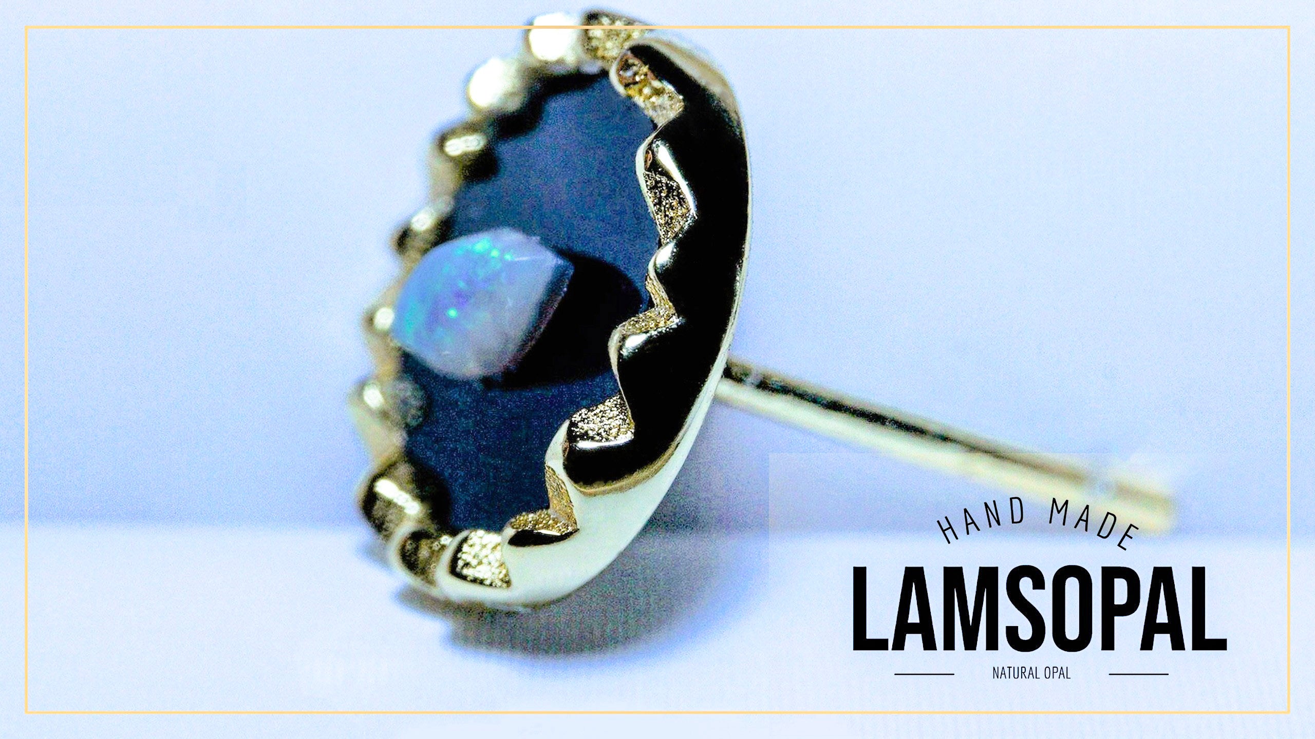 A handmade Lamsopal stud earring featuring a natural opal in a bezel setting with black enamel and gold accents, shown on a light blue background with a brand logo overlay.
