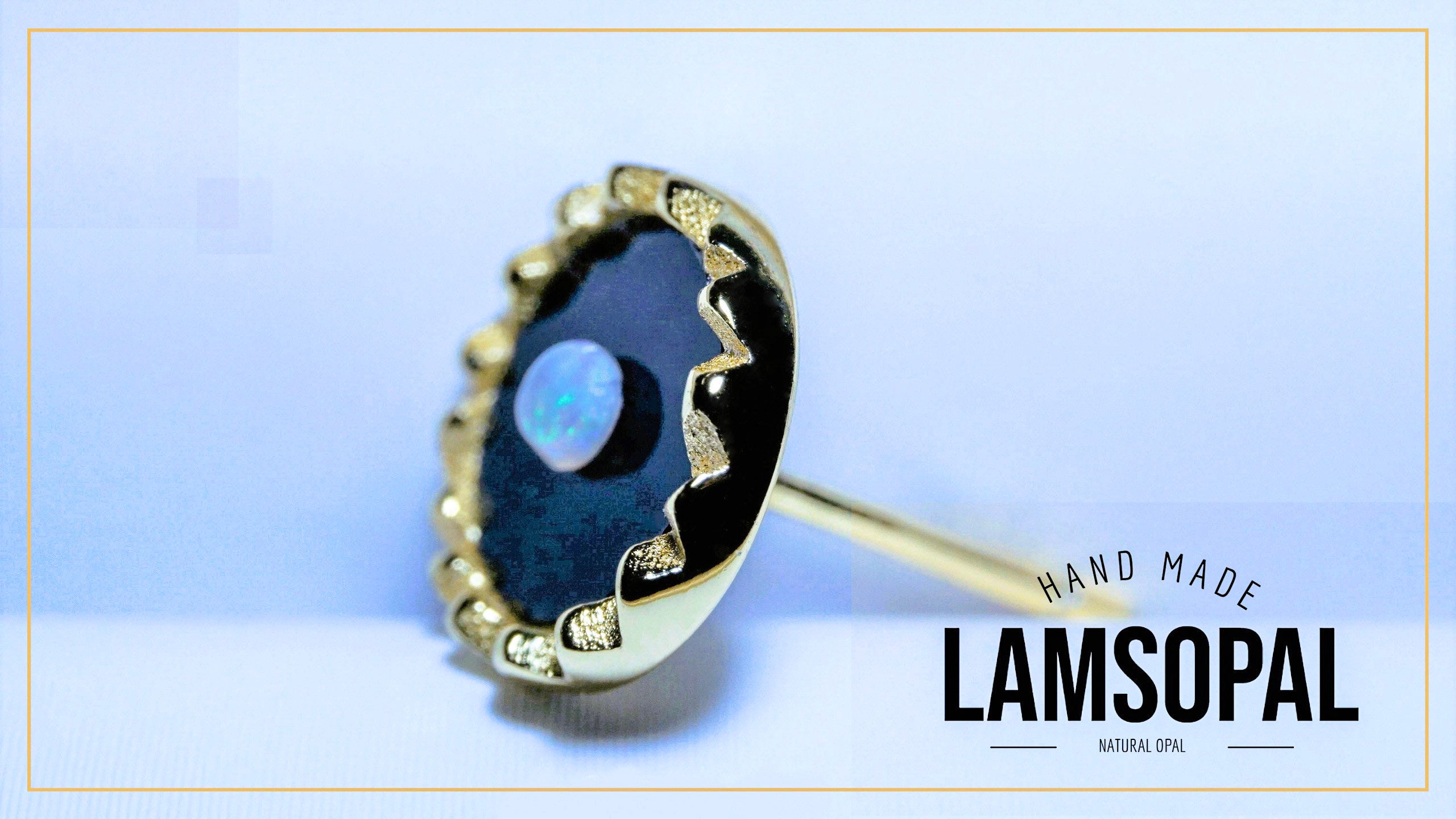 A single Lamsopal stud earring featuring a natural opal inlay with a blue iridescent center surrounded by a black and gold scalloped bezel setting. The brand name 'LAMSOPAL' is visible in the bottom right corner.