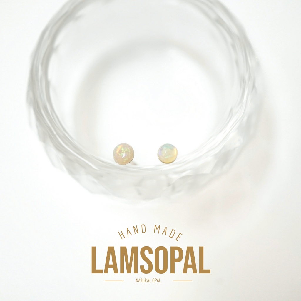 Two small iridescent natural opal stud earrings displayed inside a clear textured glass bowl on a white background, with the text 'HAND MADE LAMSOPAL NATURAL OPAL' below.