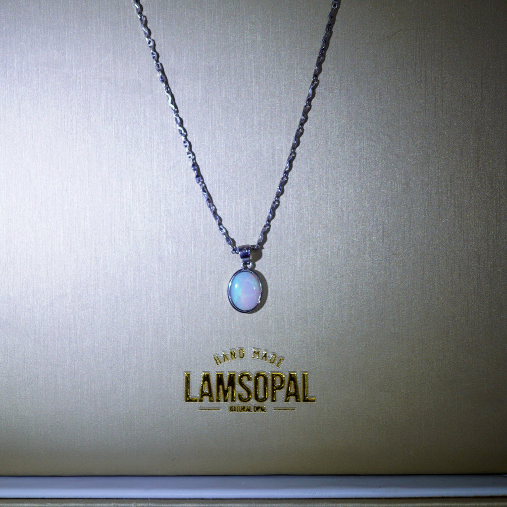 A silver-toned chain necklace with an oval iridescent pendant displayed on a textured beige background with the Lamsopal brand name printed below.