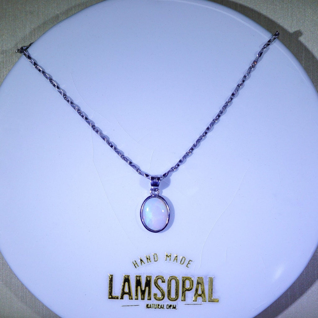 A silver-toned chain necklace with an oval pendant featuring a milky white iridescent stone, displayed on a white circular stand with the brand name Lamsopal visible at the bottom.
