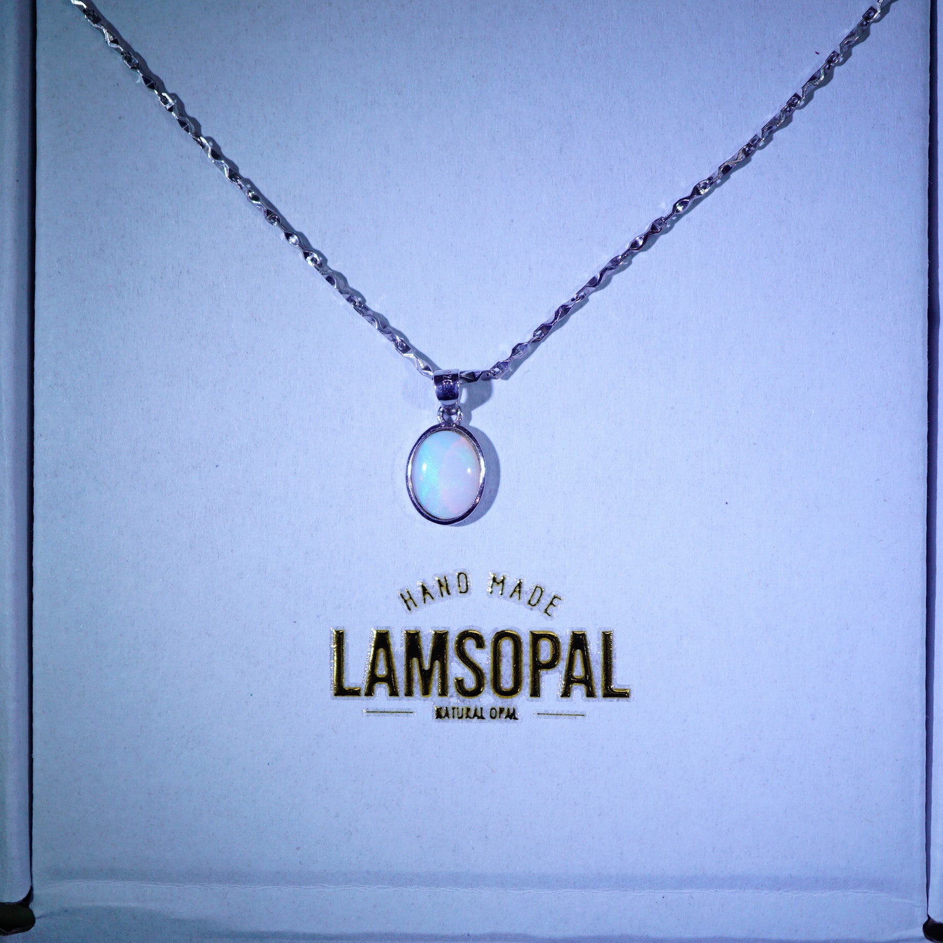 A silver chain necklace with a round iridescent white pendant displayed on a light blue backing card. The card features the brand name 'LAMSOPAL' printed in gold.