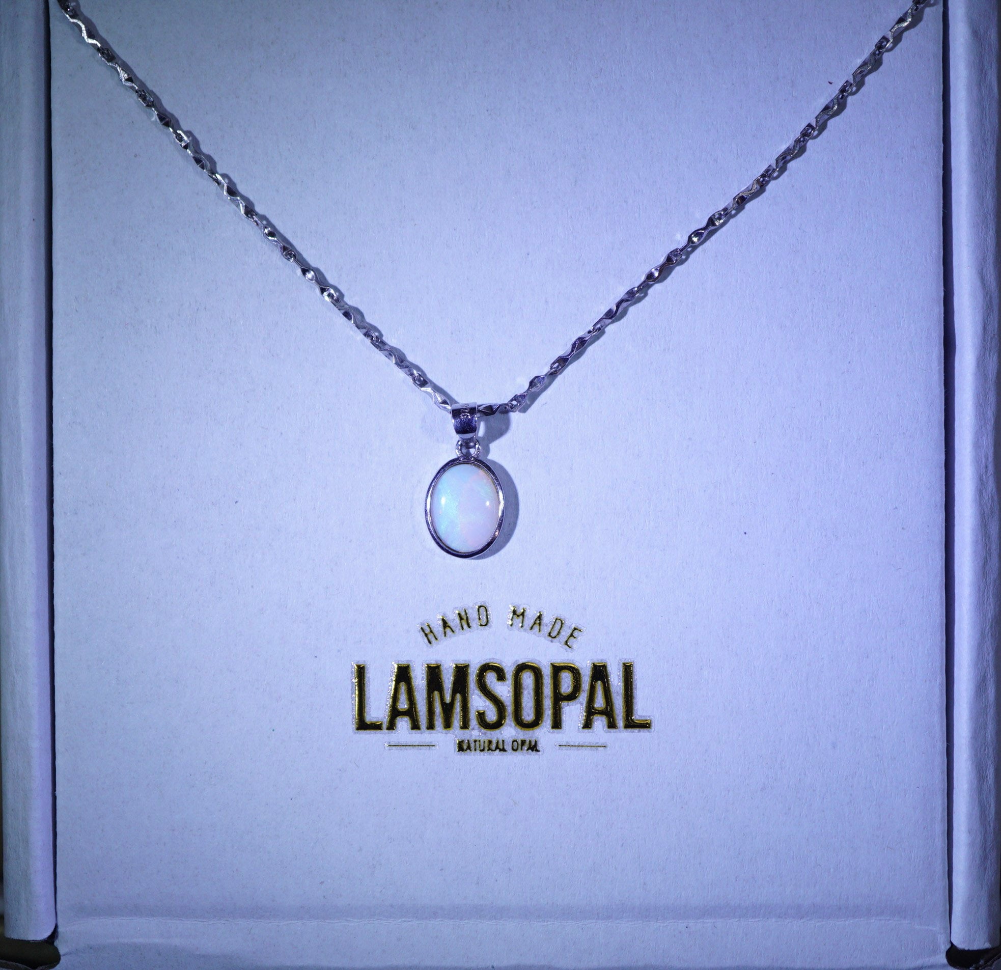 A silver chain necklace with a circular white opal pendant displayed inside a branded Lamsopal gift box.
