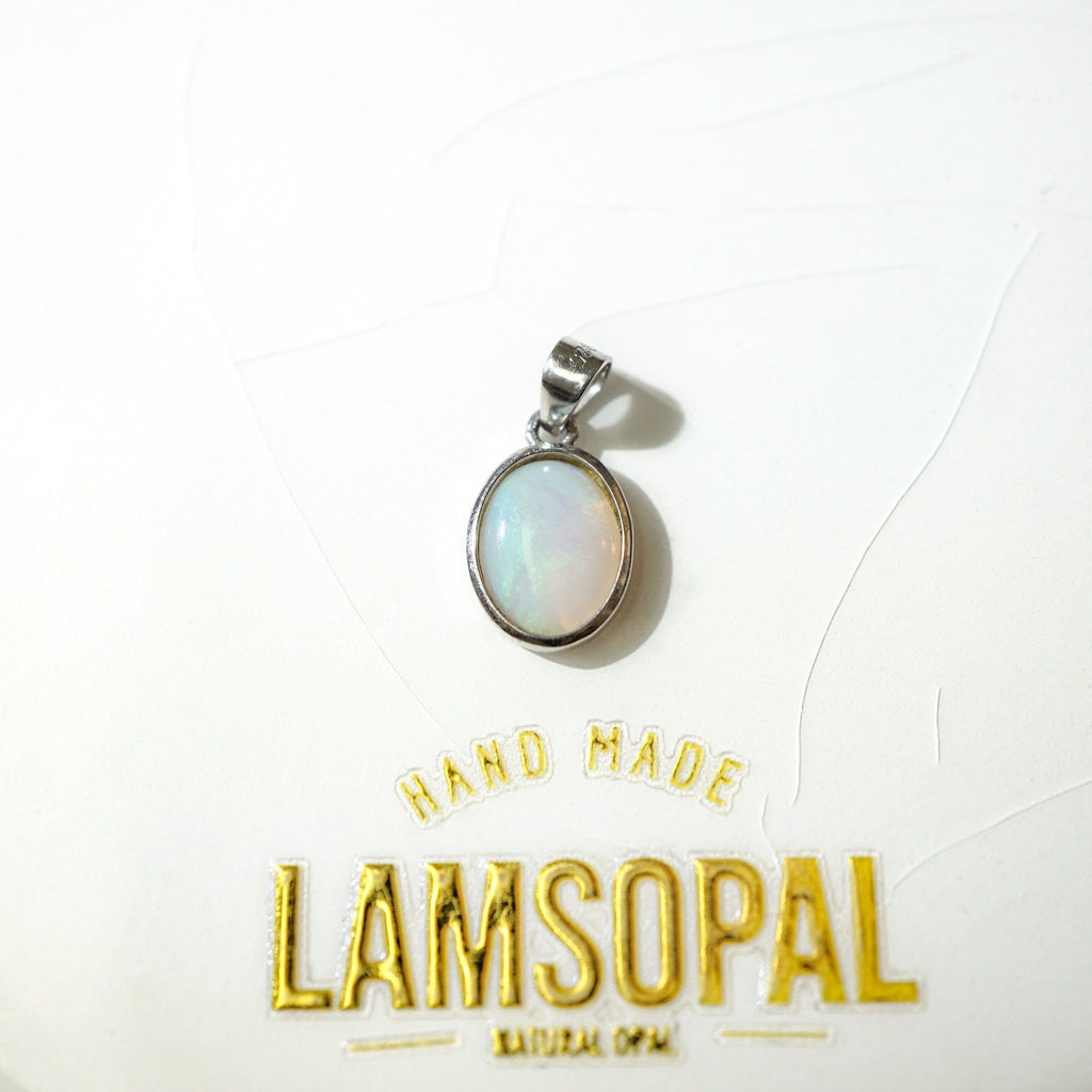 A silver oval pendant with a milky white iridescent opal stone, displayed on a white textured background with gold foil branding that reads 'HAND MADE LAMSOPAL NATURAL OPAL'.
