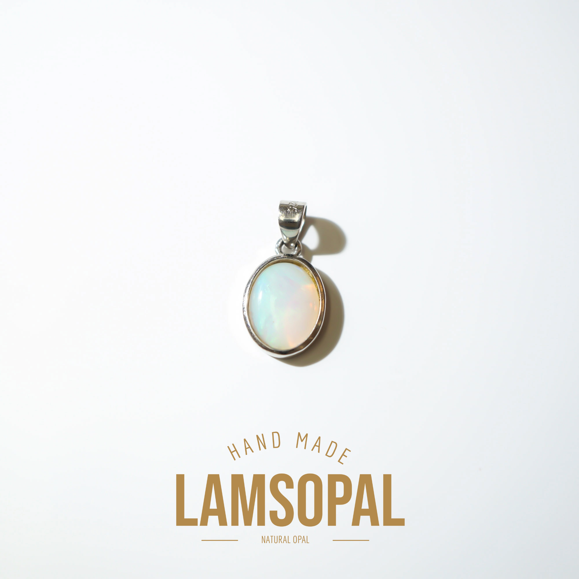 A silver pendant with a round iridescent natural opal cabochon, displayed on a clean white background with a soft shadow. Below the pendant, the text 'HAND MADE LAMSOPAL NATURAL OPAL' is written in gold-colored lettering.