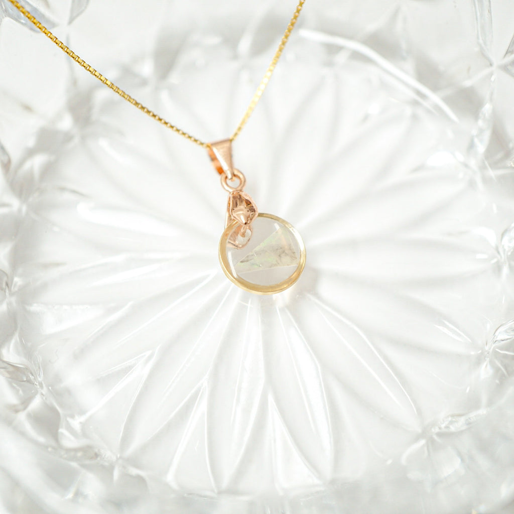 A delicate gold chain necklace with a rose gold pendant featuring a clear glass orb containing a small white butterfly, displayed on a textured white glass plate.