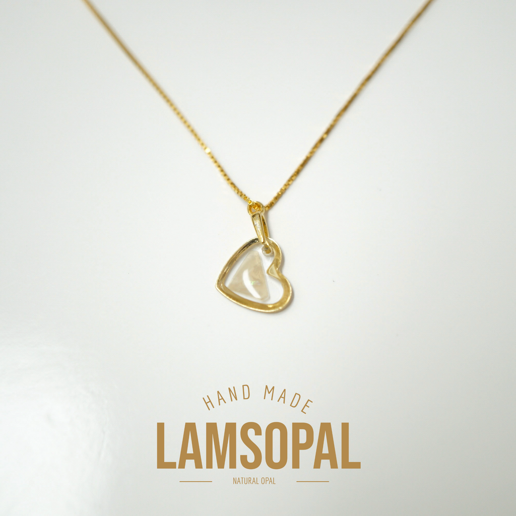 A gold heart-shaped pendant necklace with a clear, polished inlay, displayed on a white background with a gold 'LAMSOPAL HAND MADE' logo overlay at the bottom.