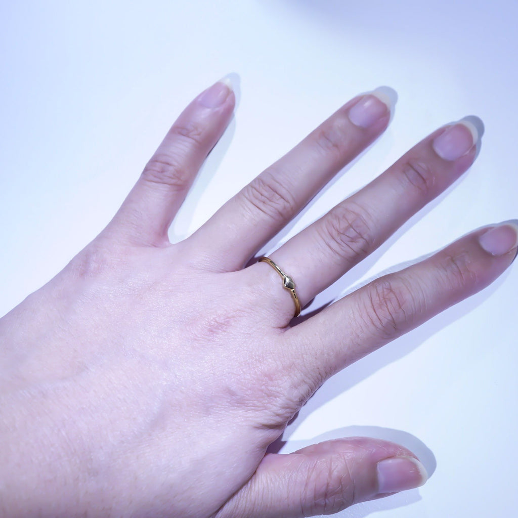 A close-up of a hand wearing a thin gold band ring on one of the middle fingers, set against a plain white background.