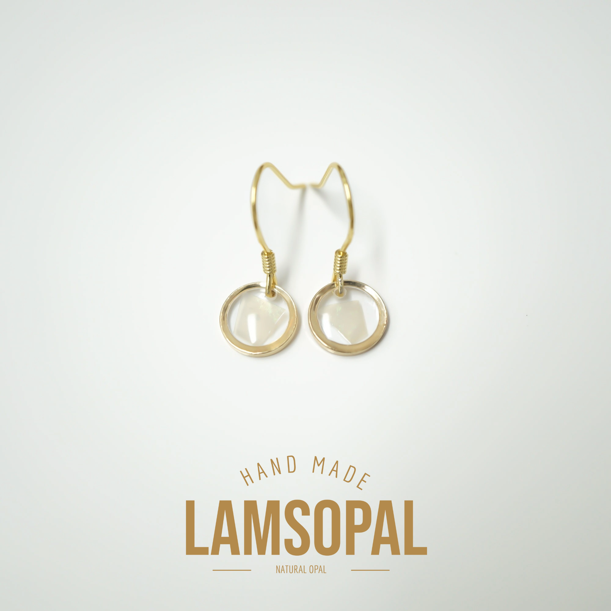 A pair of gold-tone drop earrings with circular natural opal charms, displayed on a clean white background with a gold 'LAMSOPAL' brand logo and 'HAND MADE' text below.