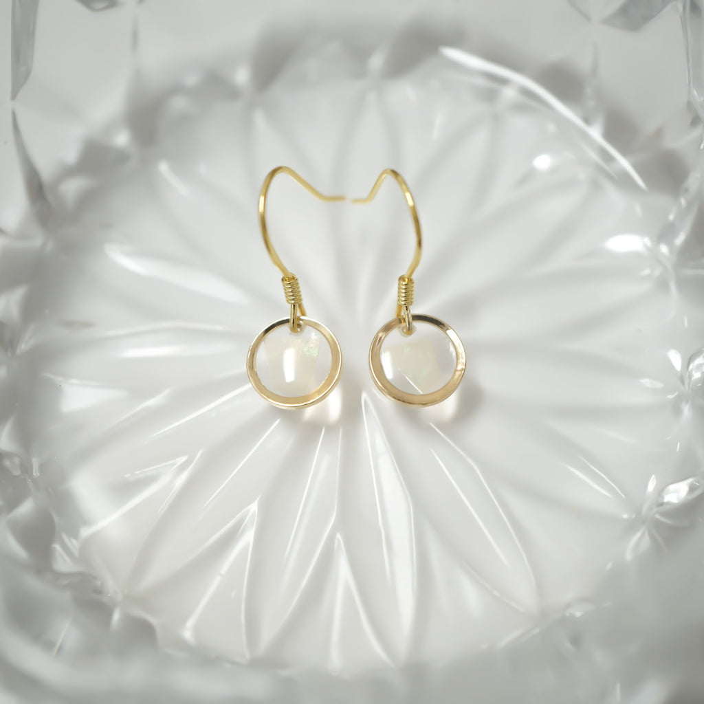 A pair of gold hoop earrings with circular white inlay details, displayed on a textured white glass dish.