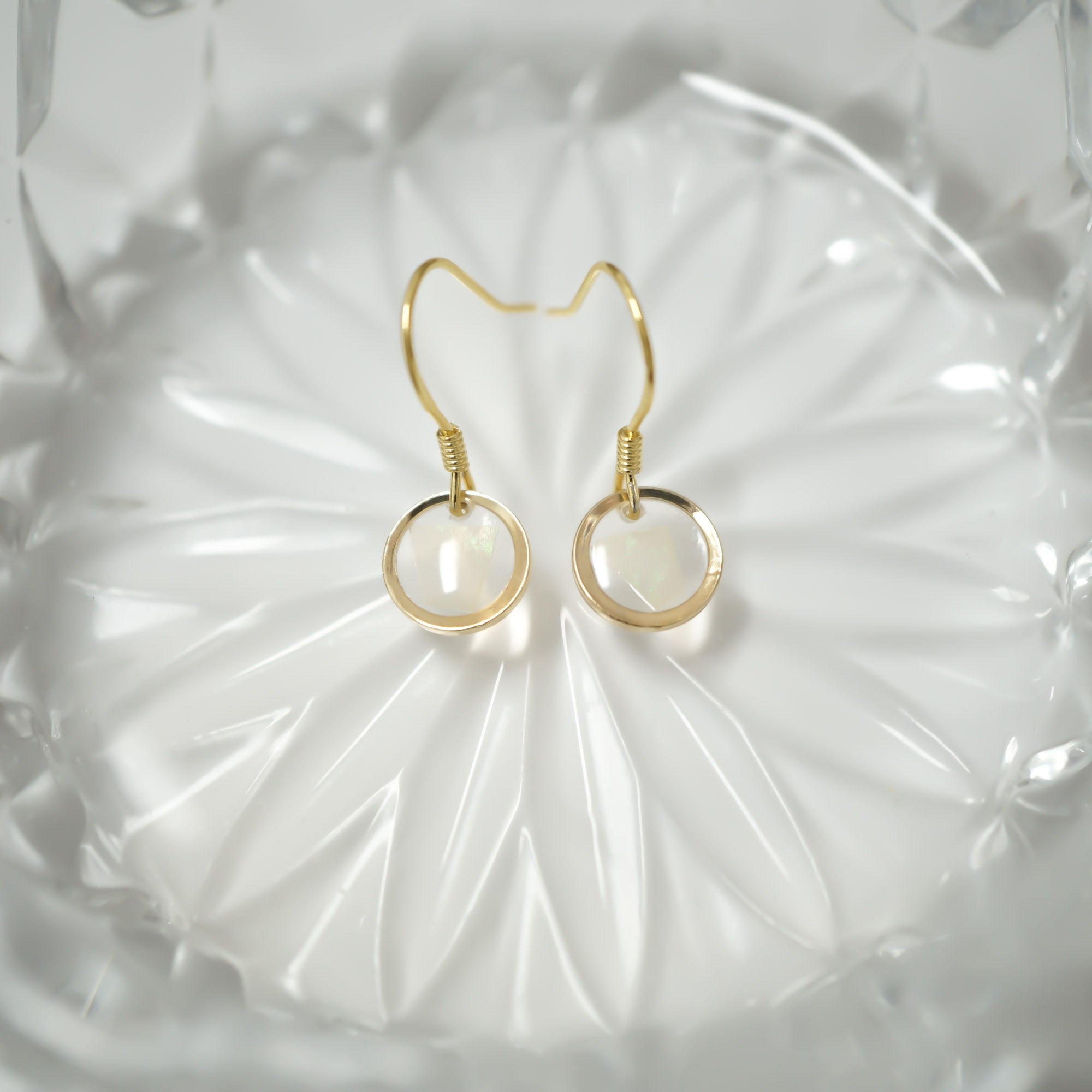 A pair of gold hoop earrings with circular white inlay details, displayed on a textured white glass dish.