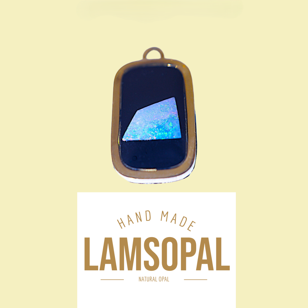 A rectangular natural opal pendant with a gold-toned bezel and loop, shown above a white label that reads 'HAND MADE LAMSOPAL NATURAL OPAL' on a pale yellow background.
