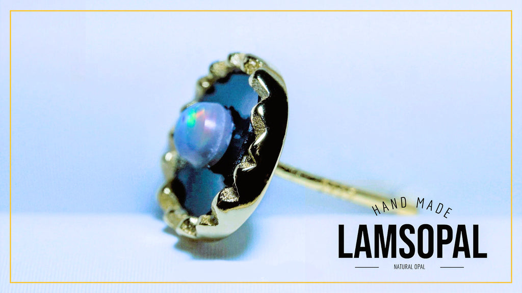 A handmade Lamsopal natural opal ring with a gold bezel setting, displayed on a light blue background with a gold border and brand text overlay.